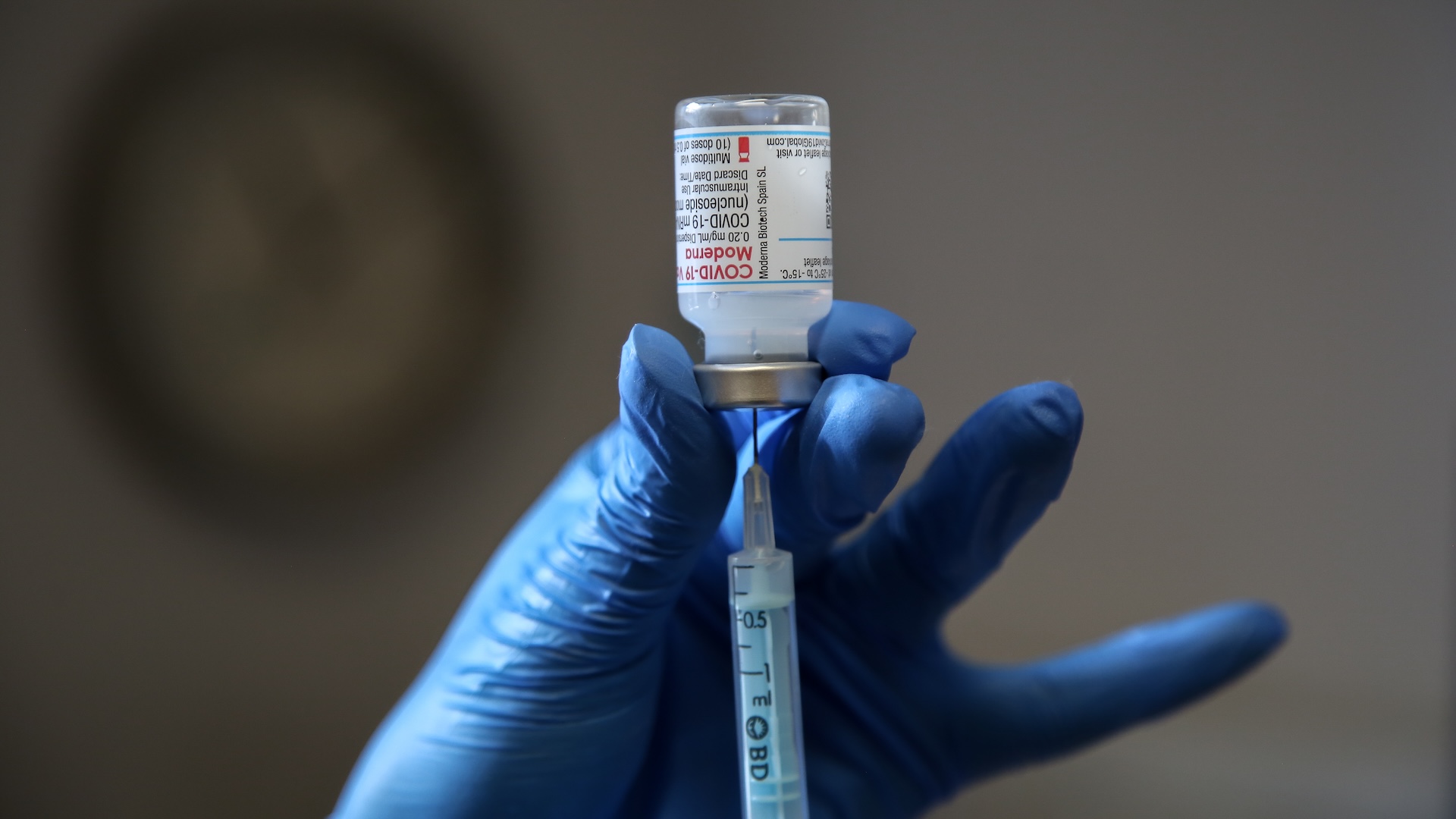 a gloved hand uses a syringe to withdraw a dose of mRNA COVID vaccine from a vial