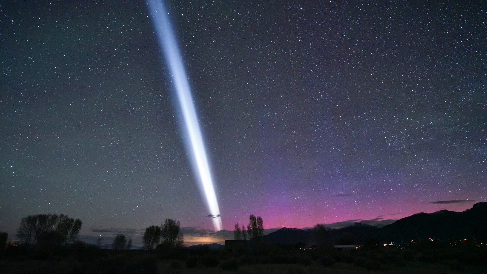A white streak of light in the night sky with purple auroras visible in the background