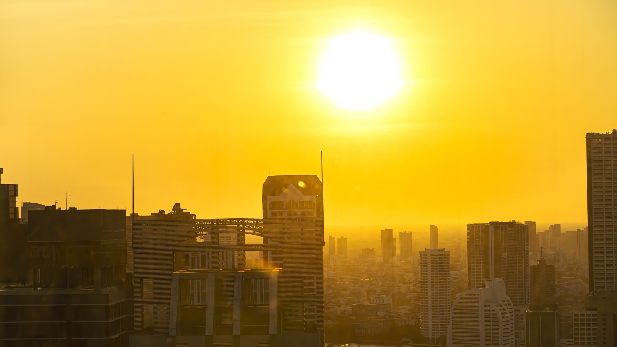 A cityscape with a very large, bright sun shining over it.