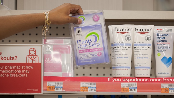 A hand picks up a package of Plan B One-Step from a pharmacy shelf.