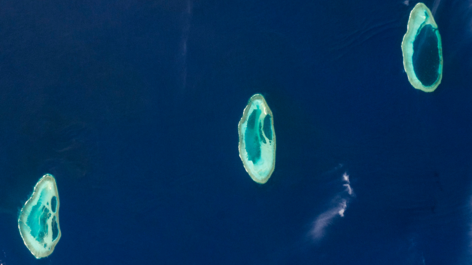 Satellite photo of three oval-shaped atolls in a straight line in the ocean