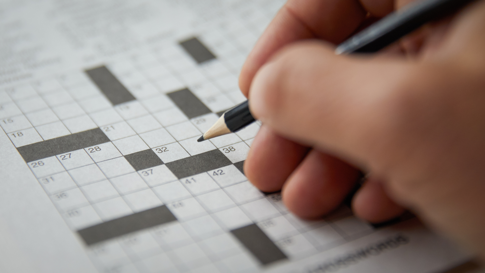 A hand holding a pencil over a crossword puzzle