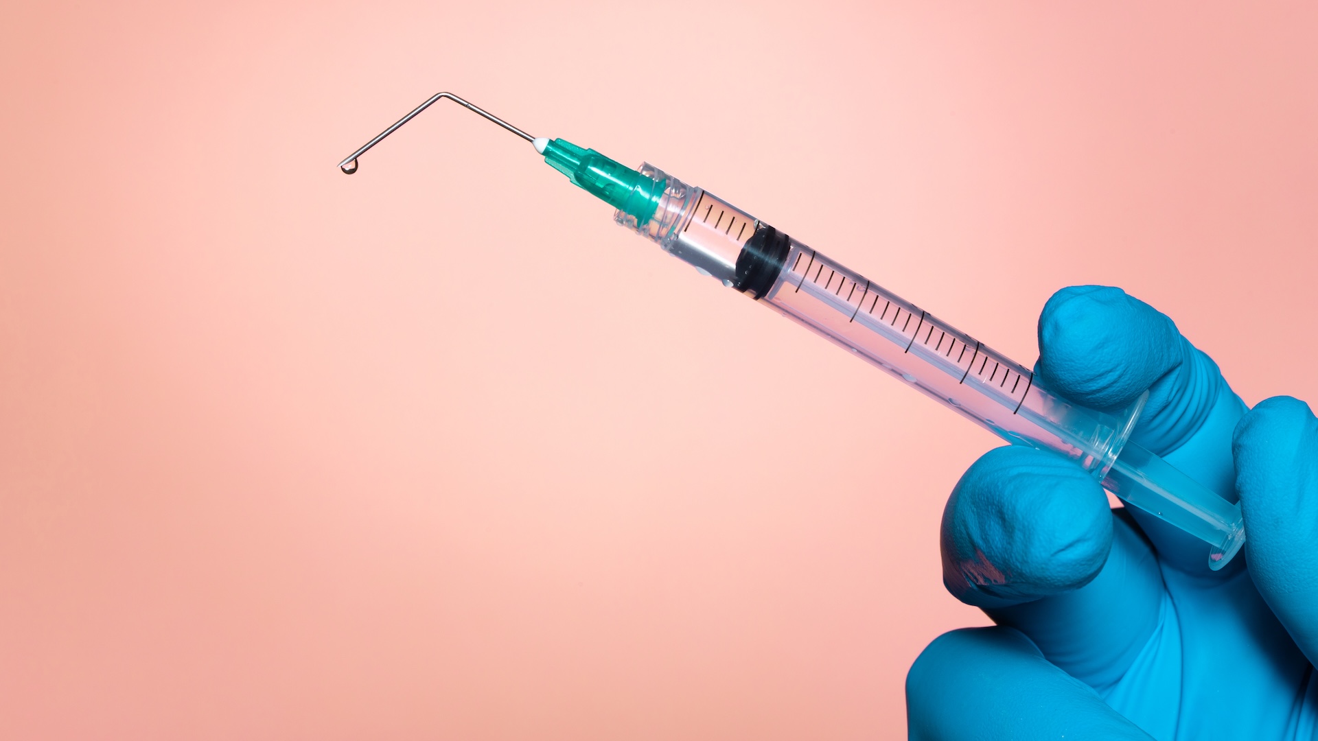 A photo of a gloved hand holding a syringe with a broken needle