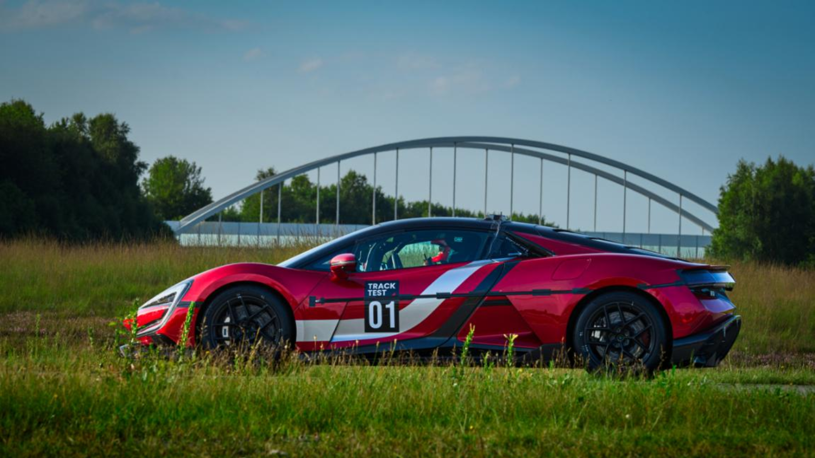 The YANGWANG U9 Track Edition fully electric supercar on grass with a bridge in the background.